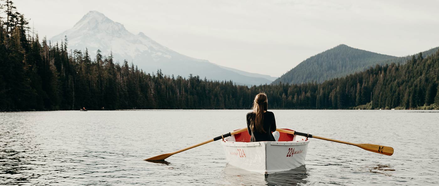 woman on lake in a row boat facing mountains